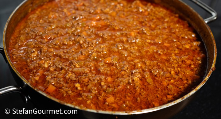 A large pot of simmering Bolognese sauce with finely chopped vegetables and ground meat, showcasing rich colors and texture.