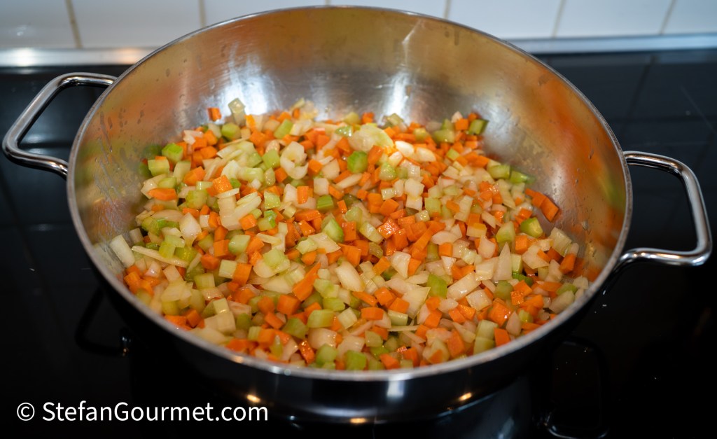 Chopped vegetables including carrots, celery, and onions in a large pot.
