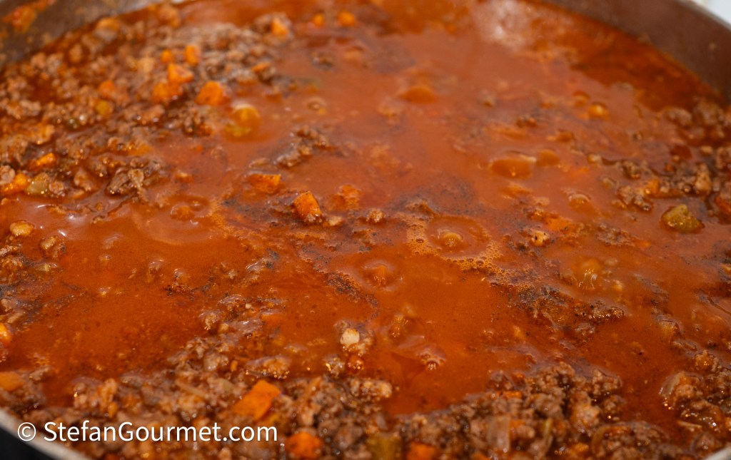 A close-up of simmering ragù, showcasing a rich tomato sauce with ground meat and vegetables.