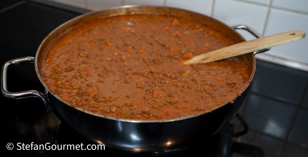 A pot of simmering ragù alla Bolognese with a wooden spoon resting on the edge.
