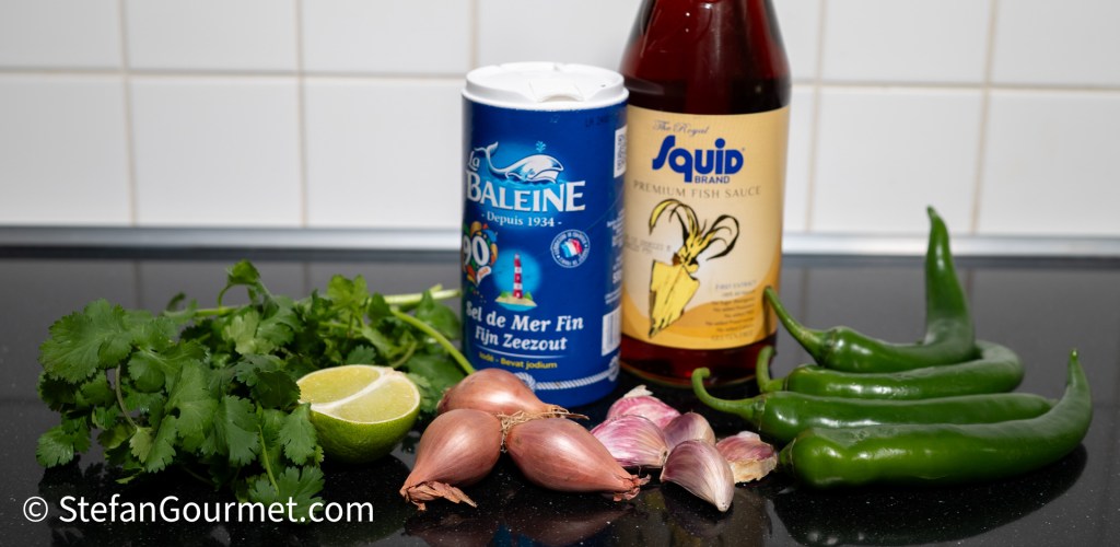 An assortment of ingredients for a Thai dip, including fresh cilantro, lime, shallots, garlic, green chili peppers, coarse salt, and fish sauce.