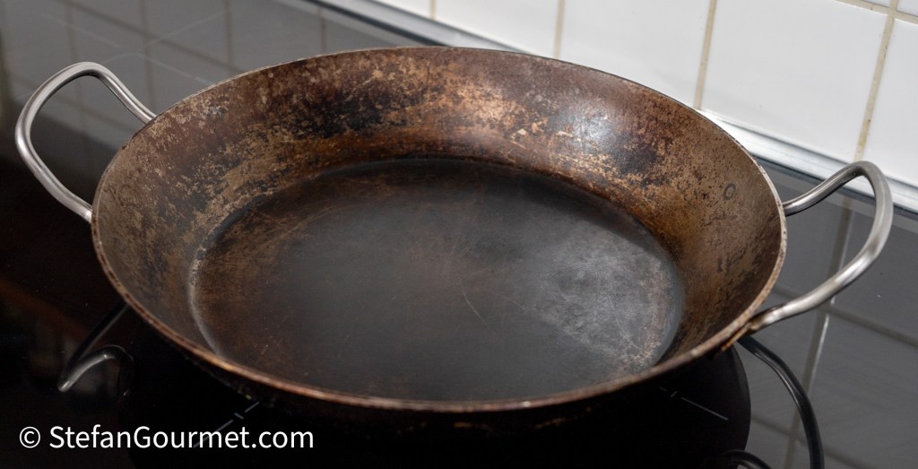 An empty, round frying pan with two side handles, placed on a stovetop.
