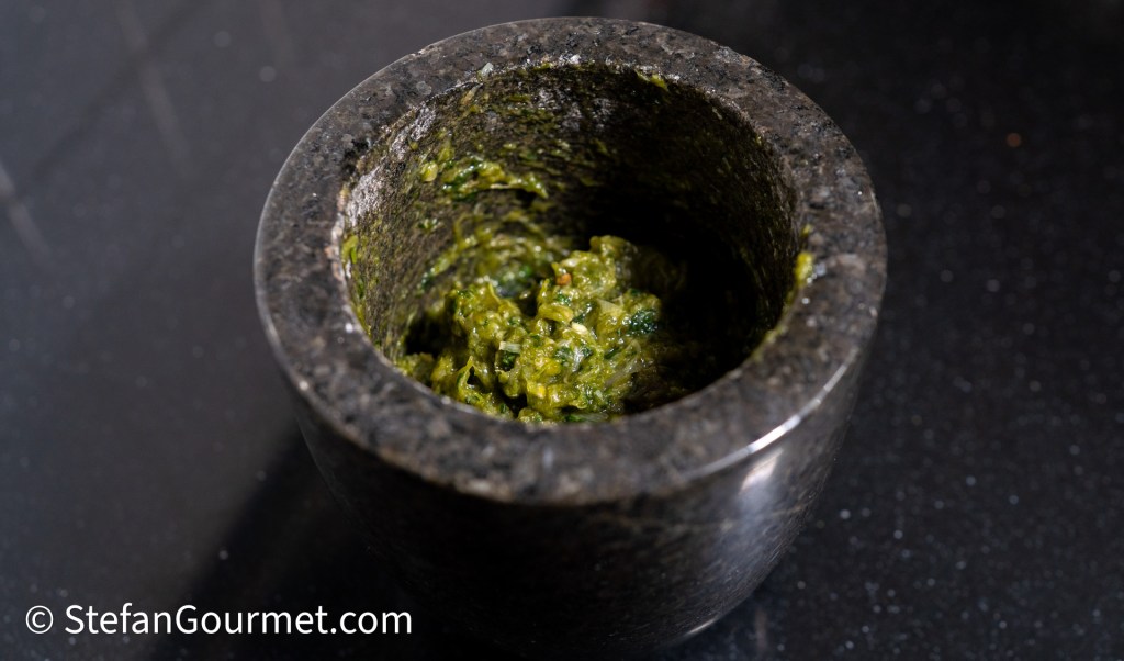 A mortar filled with a green chili dip mixture, placed on a dark countertop.
