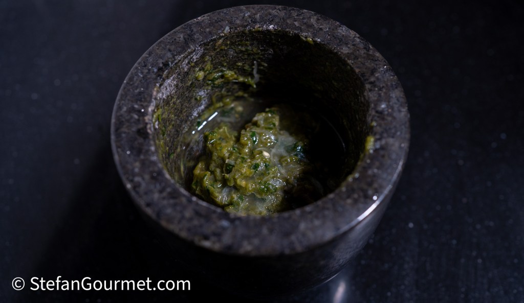 Close-up of a stone mortar filled with green chili paste, reflecting the texture of the mixture.