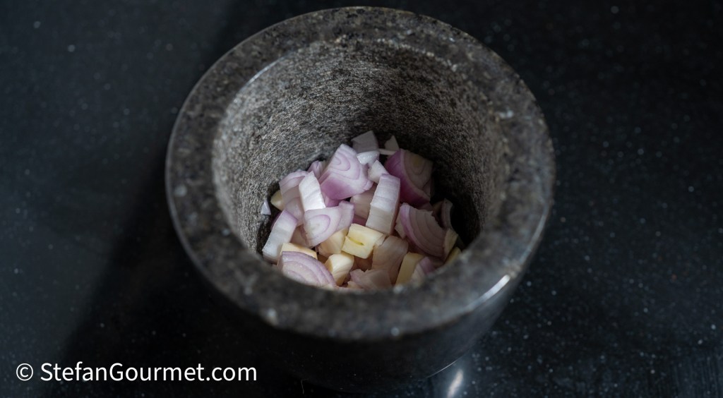 A mortar containing chopped shallots and garlic on a dark countertop.
