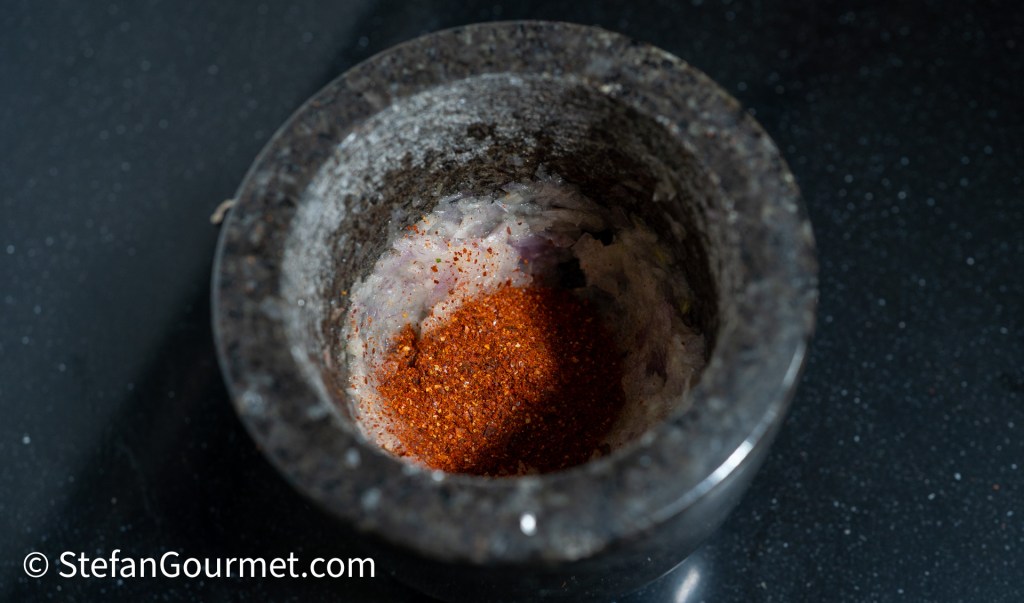 A stone mortar filled with red chili powder, sitting on a dark countertop.