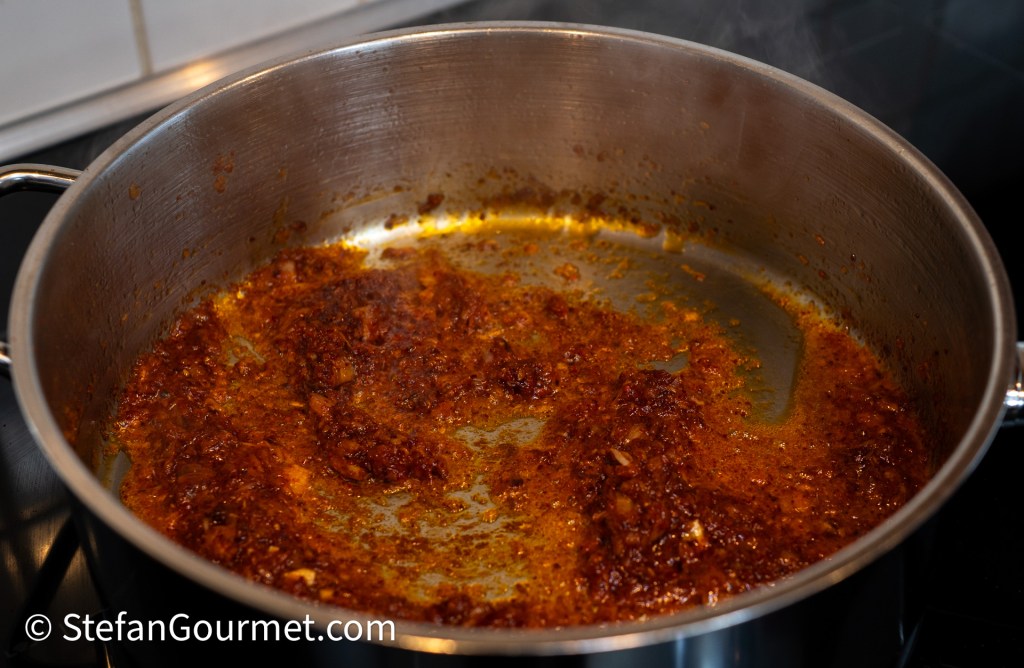 A stainless steel pot containing a rich, brown chili paste simmering on a stove.