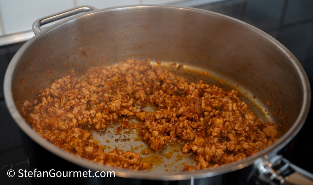 Cooked ground pork in a frying pan, mixed with spices and seasonings.