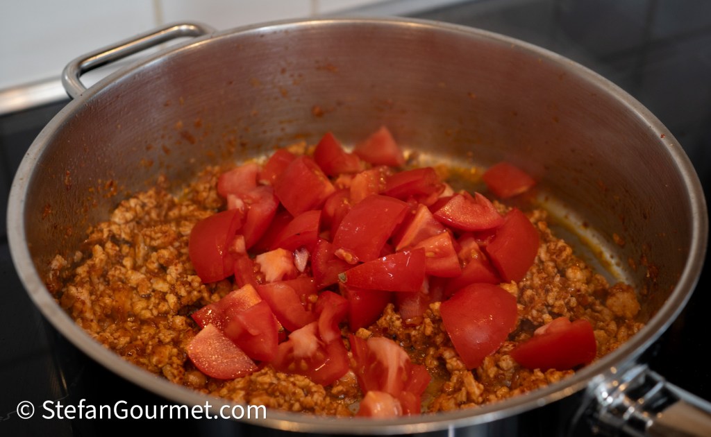 Cooking ground pork with chopped tomatoes in a stainless steel pan.