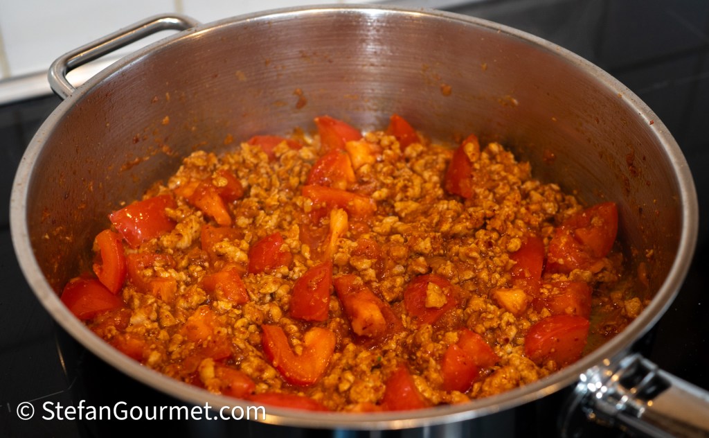 A pot containing a mixture of ground pork and chopped tomatoes, simmering together to create a flavorful dish.