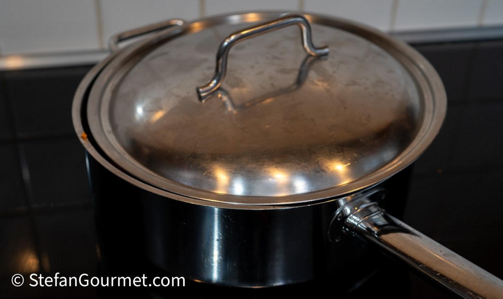 A stainless steel pot with a lid, placed on a black stovetop.
