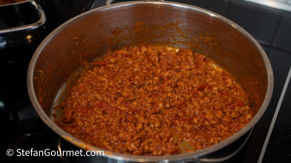 A pot containing Nam Phrik Ong, a Northern Thai dip made with ground pork and tomatoes, simmers on a stovetop.