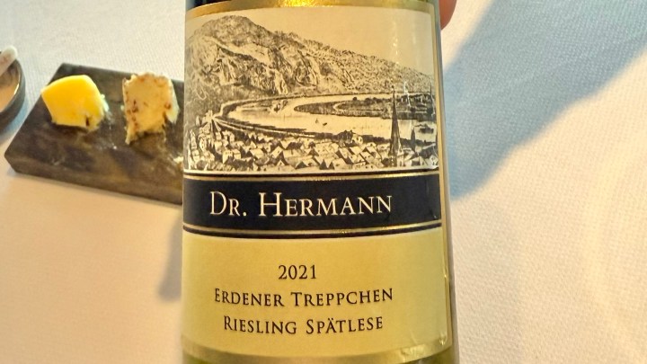 A close-up of a wine bottle labeled 'Dr. Hermann 2021 Erdener Treppchen Riesling Spätlese', alongside a small dish with butter and a cheese ball on a slate plate.