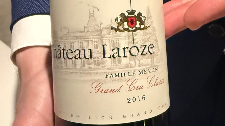 Close-up of a hand holding a bottle of 2016 Château Laroze wine, featuring a detailed label with text and an illustration of the château.