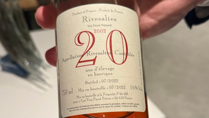 A close-up image of a Rivesaltes wine bottle showing its label with details including the year 2002, and information about its aging process and alcohol content.