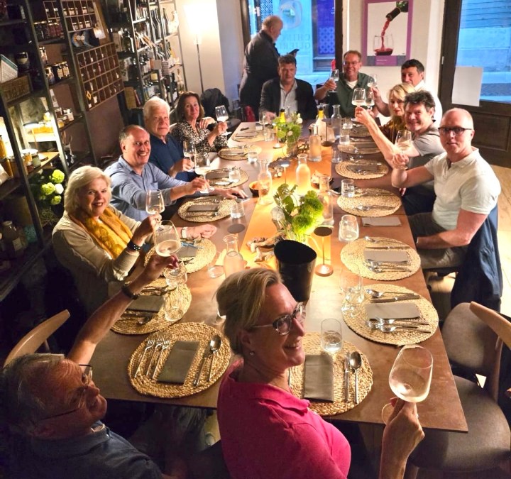 A group of people gathered around a dinner table, holding glasses and smiling, in a warmly lit restaurant setting.