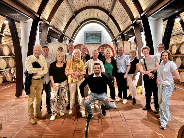 Group of wine connoisseurs posing together inside a winery with wooden barrels in the background.