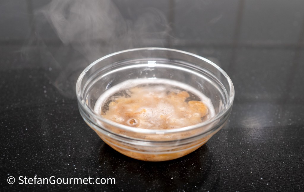 A steaming bowl of Nam Phrik Kapi dip, showcasing its rich, brownish color, placed on a black countertop.