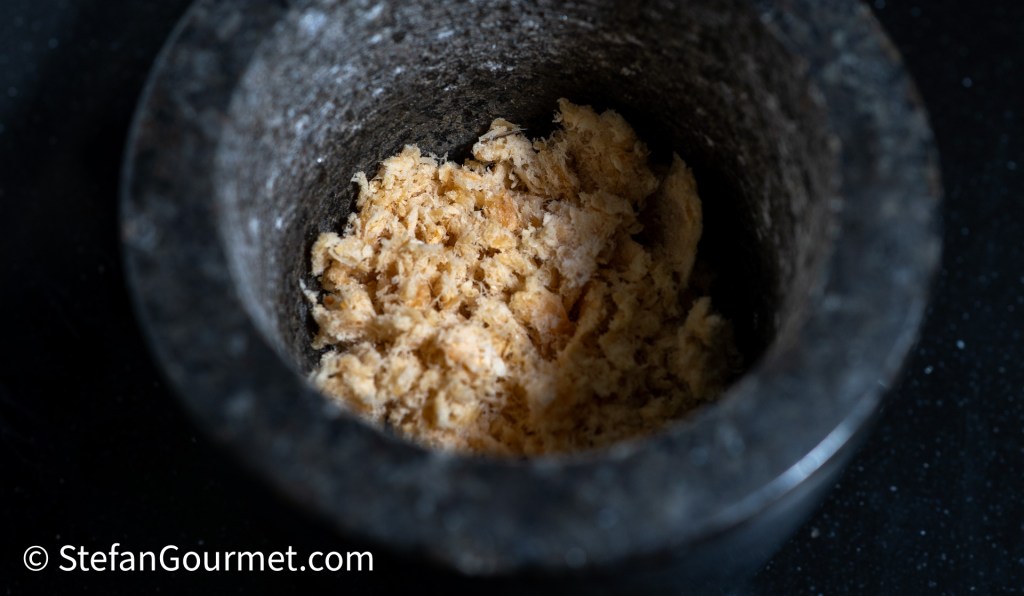 A close-up of pounded dried shrimp in a mortar, showcasing its fluffy texture against a dark background.