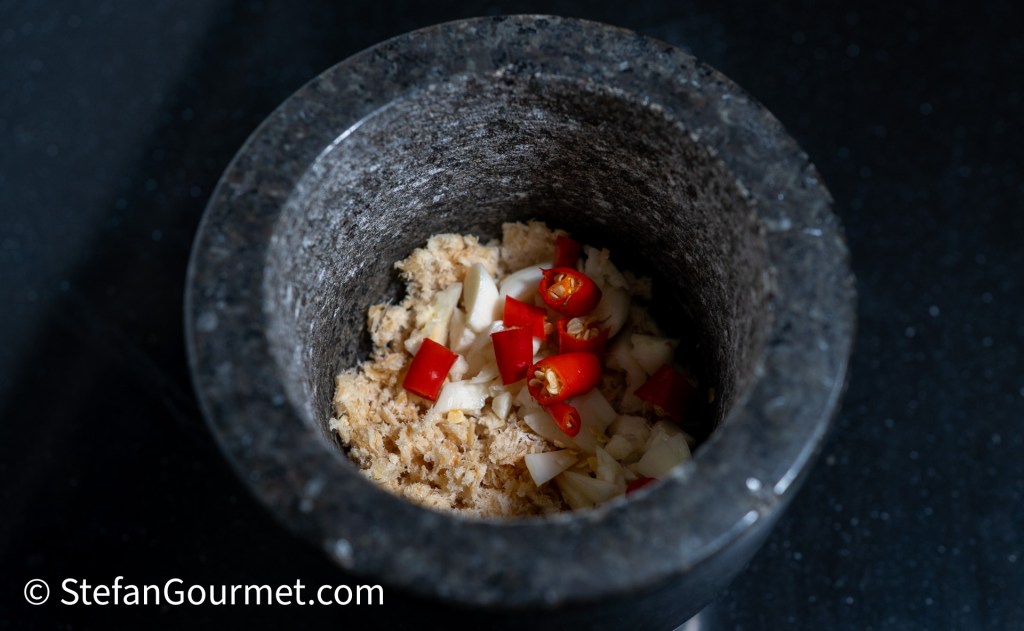 Mortar filled with pounded dried shrimp, garlic, and red Thai chilies, set against a dark background.