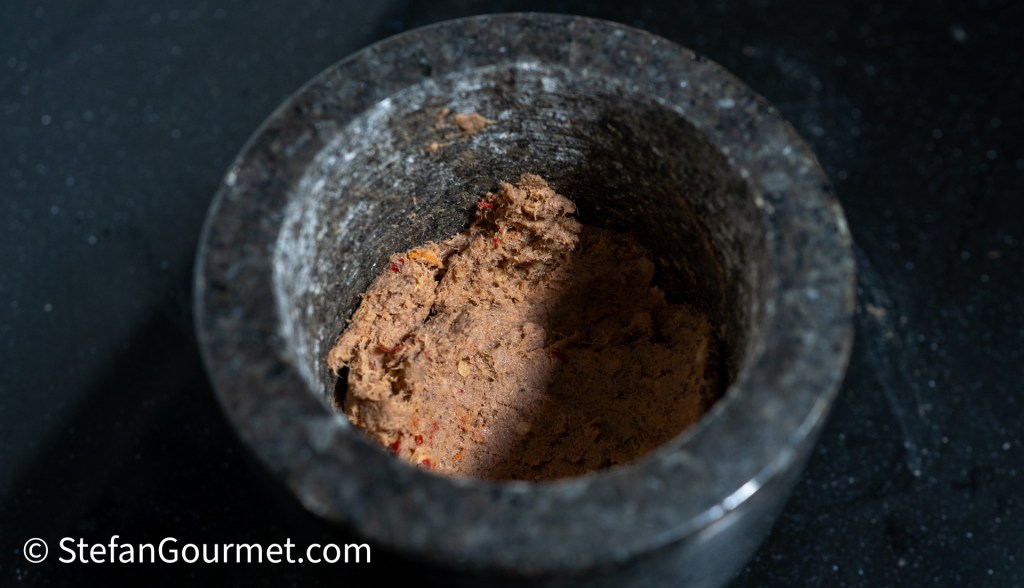 A stone mortar filled with a thick, brownish Thai chili paste, showcasing the texture and ingredients of a traditional Nam Phrik dip.