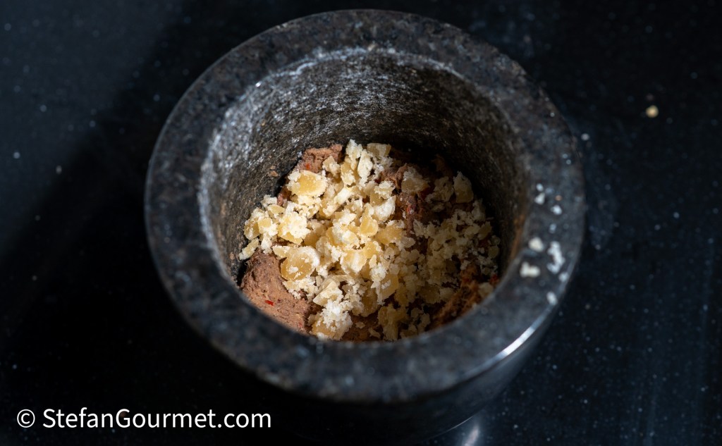 Close-up of a mortar filled with shrimp paste and palm sugar, used for preparing Nam Phrik Kapi, a Northern Thai dip.