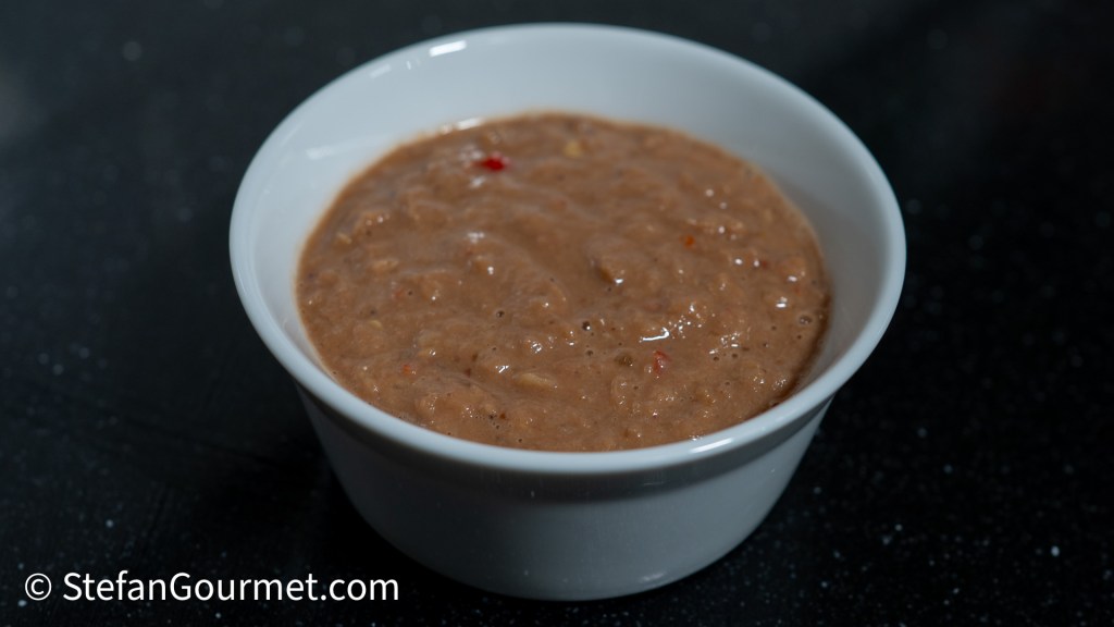 A small bowl containing Nam Phrik Kapi, a spicy Thai shrimp paste dip, with a smooth texture and small red chili flakes visible on top.