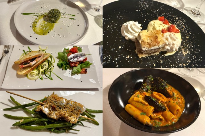 A beautifully arranged plate featuring a variety of dishes, including a green vegetable appetizer, a red mullet sandwich with salad, a sardine skewer with green beans, and a rich pasta dish in a savory sauce. A dessert with cream and strawberries is also included.