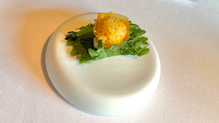 An elegant appetizer featuring a shiso leaf topped with trout roe and a delicate egg yolk, presented on a white plate.