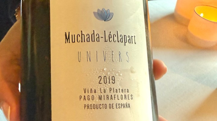 Close-up of the 2019 Univers wine bottle by Muchada-Léclapart, featuring a clean label with a lotus flower logo, held by a person in a restaurant setting.