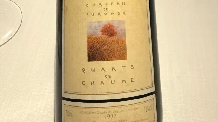 Close-up of a bottle of 1997 Quarts de Chaume by Chateau de Suronde, featuring a distinctive label with a tree and vineyards.
