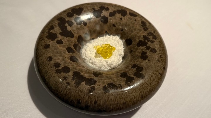 A decorative dish featuring a textured surface and a central mound of fine white powder with bright yellow crystals on top, presented elegantly on a white tablecloth.