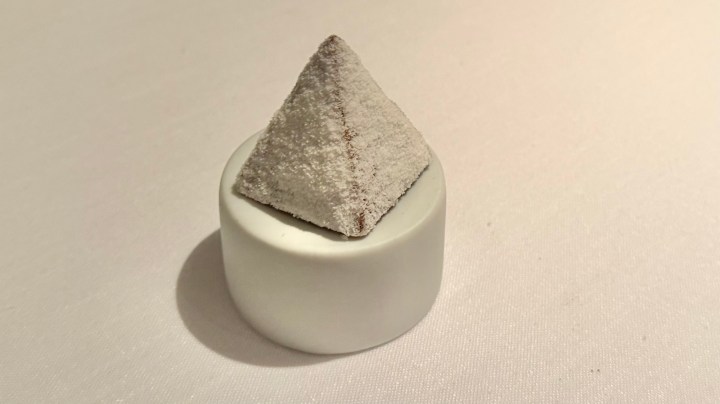 A white pyramid-shaped dessert resting on a small round plate, featuring a textured surface.