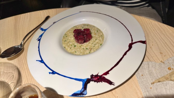 A plate featuring creamy risotto topped with diced raw tuna and a drizzle of colorful sauces, set on a wooden table.