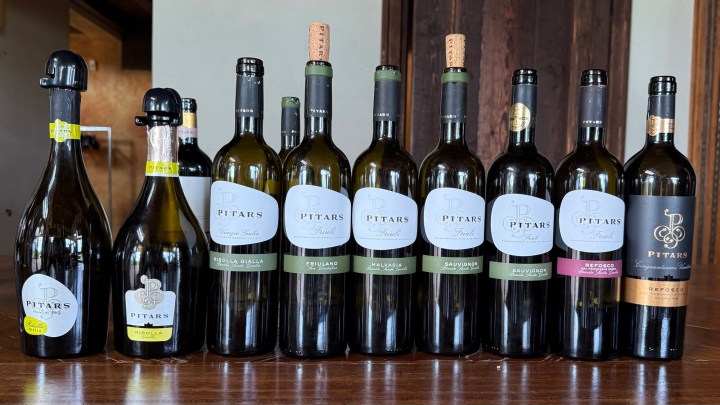 A display of various wine bottles from the Pitars winery, showcasing different labels including Ribolla Gialla, Sauvignon, and Refosco on a wooden table.