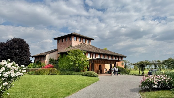A picturesque winery building surrounded by well-kept gardens and flower beds under a cloudy sky.