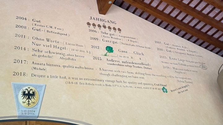 A wall showcasing vintage harvest quality notes in multiple languages, with a decorative emblem at the bottom.