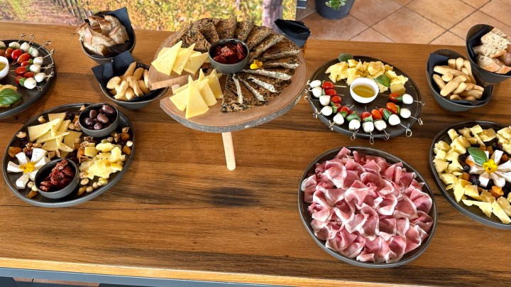 A selection of local cheeses, cured meats, olives, breadsticks, and fresh vegetables arranged on wooden platters, showcasing a variety of traditional snacks typical for a wine tasting meal.