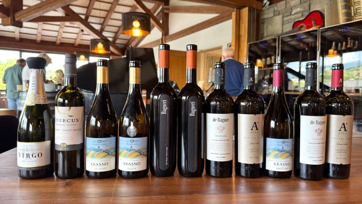 A display of various Slovenian wines on a wooden table, including bottles from De Baguer, Krasno, and Quercus, with a cozy winery interior in the background.