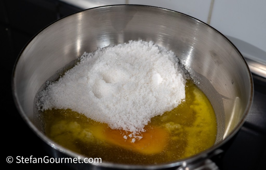 A stainless steel bowl with melted butter, sugar, and an egg yolk for dessert preparation.