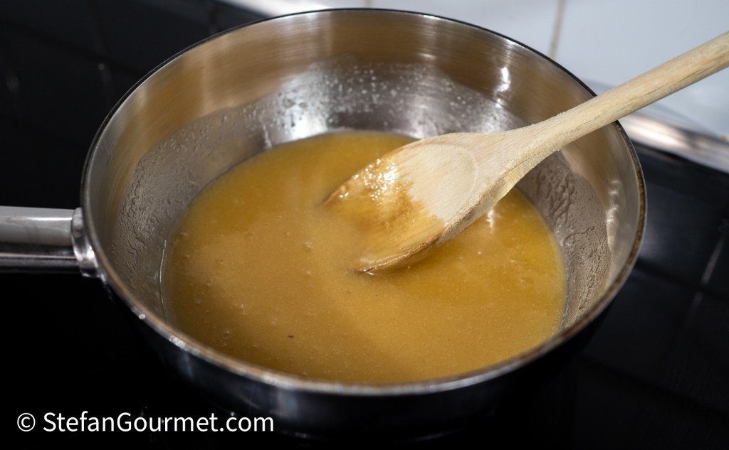 A saucepan with a mixture of melted butter, sugar, and honey being stirred with a wooden spoon.