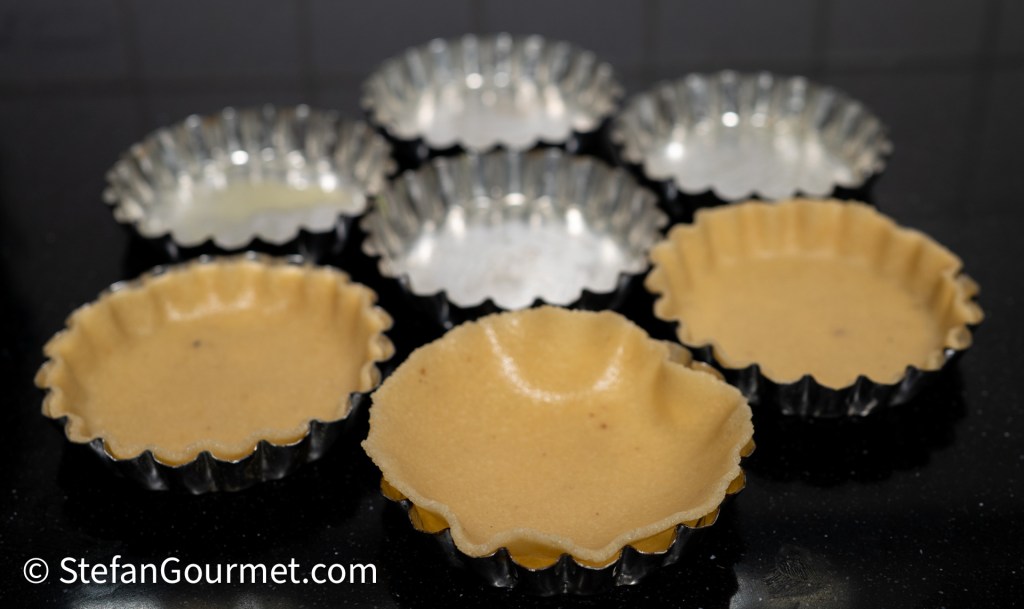 Almond dough shells shaped in metal tart molds, ready for baking.
