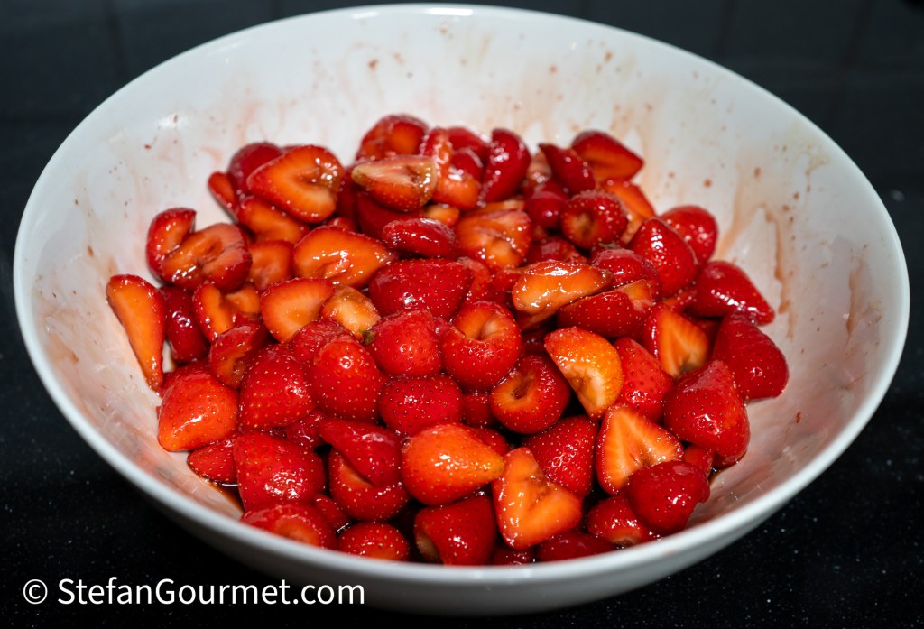 A bowl filled with macerated strawberries, showcasing halved and whole berries coated in a glossy glaze.