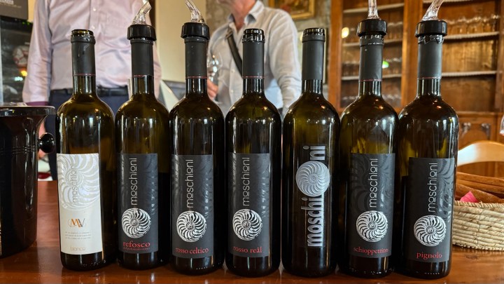 Bottles of Moschioni wines arranged on a table, featuring various labels, with a person in the background.