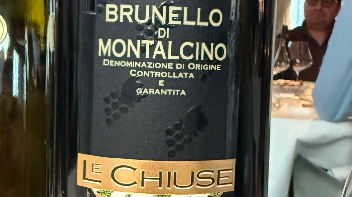 Close-up of a Brunello di Montalcino wine bottle labeled 'Le Chiuse' with details about its origin and quality.