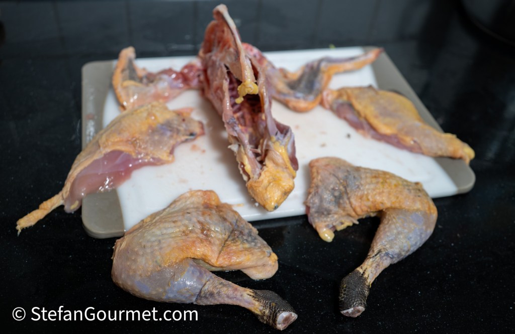 A preparation of a guinea fowl, including the carcass and separated breast fillets, legs, and wings on a cutting board.