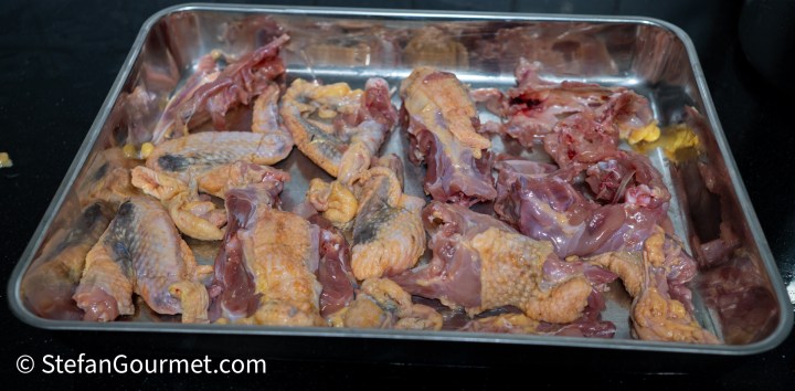 Raw guinea fowl parts including wings, carcasses, and skin arranged in a metal tray.
