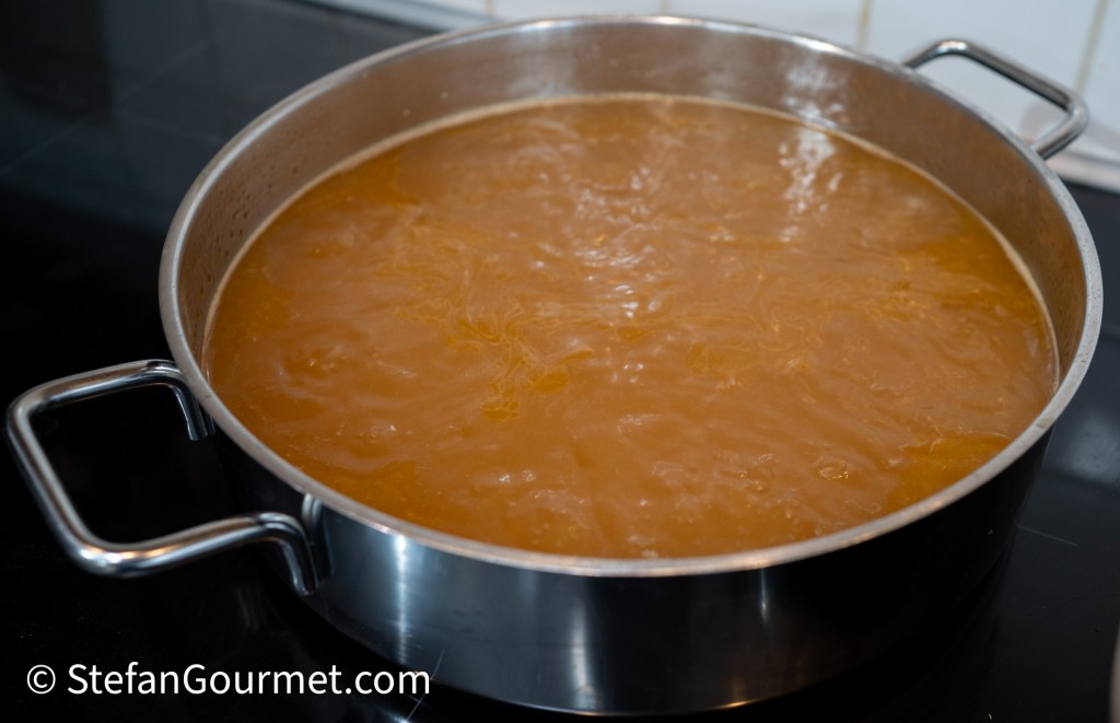 A pot of simmering guinea fowl stock on a stovetop, displayed in a stainless steel pot with a reflective surface.