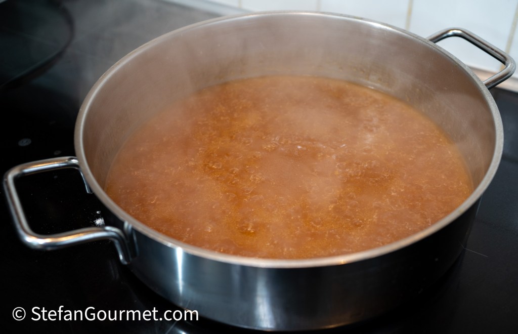A pot of simmering guinea fowl stock producing steam in a modern kitchen.
