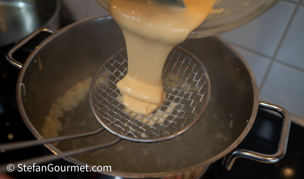 Fresh pasta batter being poured through a strainer into boiling water to make girini.
